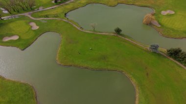 Yeşillik yeşil çayırların, kum tuzaklarının ve bulutlu gökyüzünün altında birkaç yapay gölün bulunduğu yemyeşil bir golf sahasının geniş hava manzarası.