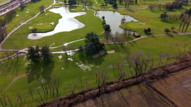 Yüksek açılı drone perspektifi, yağmurdan sonra kısmen sular altında kalan birkaç gölet ve su tehlikesi olan güzel yeşil bir golf sahasının üzerinde uçuyor.