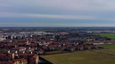 Bulutlu bir gökyüzünün altında yeşil tarım alanlarının çevresindeki konut evleri ve sanayi bölgeleri ile geniş bir Avrupa kasabası manzarası