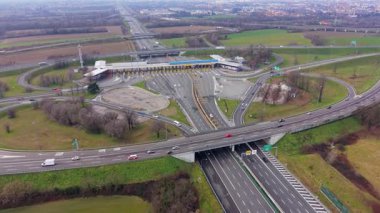 Yüksek açılı insansız hava aracı, işlek bir otoyol gişesinde ve kırsal alanda karmaşık bir yol kavşağında hareket eden araç trafiğini yakalıyor.