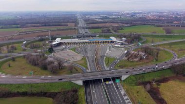 Birden fazla şeridi ve karmaşık kavşağı olan bir otoyol gişesi perspektifi. Araçlar ve kamyonlar sürüyor ve geçiş ücreti ödüyor