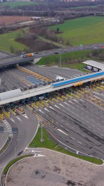 Arabalar ve kamyonlar büyük bir otobandaki modern bir gişeden geçiyorlar. Yüksek açılı perspektif geçiş gişelerinden geçen trafiği gösteriyor