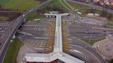Yoğun bir gişeden geçen ve kesişen otoyol üst geçidi boyunca giden araba ve kamyonların yüksek açılı hava perspektifi