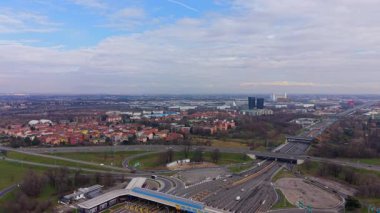 Modern bir şehrin kenar mahallelerindeki büyük bir otoyol kavşağı ve paralı yol manzarası. Otomobiller gişelerde ve yollar boyunca ilerliyor.
