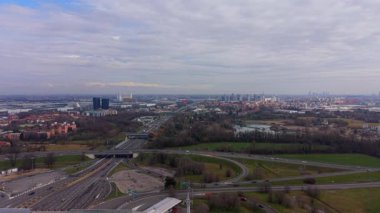 Yüksek hava görüntüsü, Milan, İtalya 'ya giriş yapan bir kavşakta otoyol trafiğini gösteriyor. Şehir silüeti bulutlu bir gökyüzünün altında uzaklardan görülebilir.