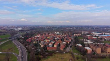 Konut alanı boyunca uzanan işlek bir otoyolun havadan görüntüsü. Arka planda panoramik şehir manzarası. Mavi gökyüzünün altında biraz bulutlu.