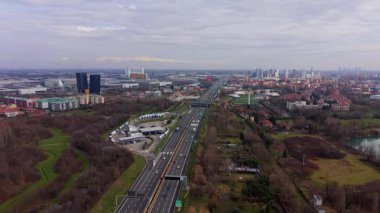 Milano, İtalya 'nın modern siluetine doğru giden yoğun bir çoklu şeritli otoyolu izleyen insansız hava aracı görüntüleri trafik ve kentsel yayılımı gösteriyor.
