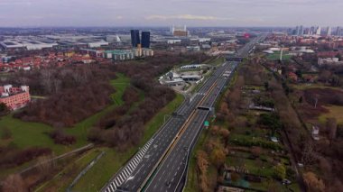 Modern bir şehir siluetine doğru akan trafiğin olduğu çok şeritli bir otoyolun havadan görünüşü. Otoyol boyunca hareket eden arabalar ve kamyonlar