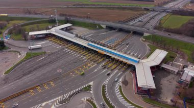 Yoğun bir otoyol gişesinden geçen arabalar ve kamyonlar. Çoklu şeritli modern yol altyapısı, ödeme kapıları ve üstgeçitleri