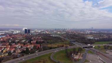 Milan, İtalya 'nın varoşlarında hareketli bir otoyol kavşağının geniş bir hava görüntüsü. Uzak kentsel ufuk çizgisine doğru hafif trafik akıyor