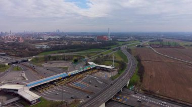 Yüksek açılı insansız hava aracı perspektifi büyük bir otobandaki kalabalık bir gişeden geçen arabaları gösteriyor. Ufukta şehrin ufuk çizgisi görünen modern altyapı ve ulaşım ağı