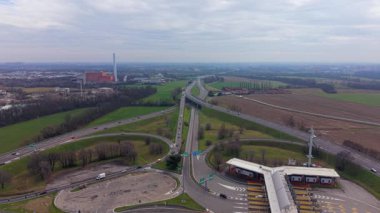 Yüksek açılı insansız hava aracı görüntüleri kalabalık bir gişede araç trafiğini ve taşra ve sanayi ile çevrili karmaşık otoyol kavşağını yakalıyor.
