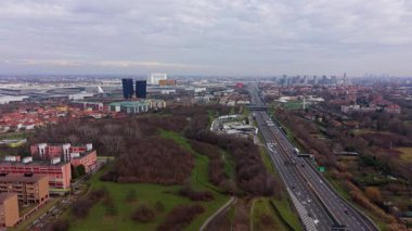 Geniş hava manzarası, Lombardiya, İtalya 'da bulutlu bir gökyüzünün altında Milan ufkuna giden çok şeritli bir otoyolda giden arabaları gösteriyor.