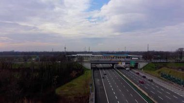 Yoğun bir otoyol kavşağından ve gişeden uzaklaşan yüksek drone görüntüsü. Bulutlu bir günde ödeme şeritlerinden geçen arabalar ve kamyonlar