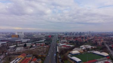 Milan, İtalya 'ya doğru yoğun bir otoyol boyunca ilerleyen İHA görüntüleri. Şehir manzarası ve ufukta görünen modern gökdelenler