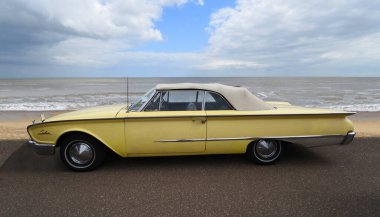 FELIXSTOWE, SUFFOLK, ENGLAND - MAYIS 07, 2017: Arka planda deniz kenarında park edilmiş klasik sarı Ford Sunliner Üstü açılabilir Araba.