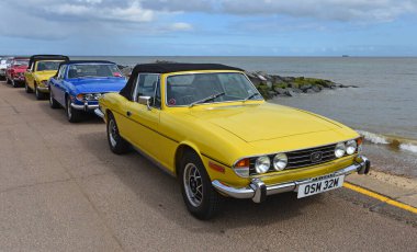 Felixstowe, Suffolk, İngiltere - Mayıs 04, 2025: Klasik sarı Triumph Stag otomobili diğer Stags 'lerle birlikte deniz kenarında park halindedir.