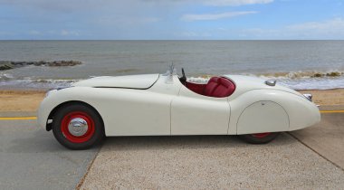 FELIXSTOWE, SUFFOLK, ENGLAND - MAYIS 04, 2025: Klasik Beyaz Jaguar XK120 Roadster arka planda deniz kenarında ve deniz kenarında park edilmiş..