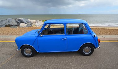 Felixstowe, Suffolk, İngiltere - 04 Mayıs 2025: Arka planda deniz kenarında park etmiş klasik Blue Austin Mini