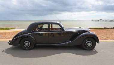 Felixstowe, Suffolk, İngiltere - 05 Mayıs 2024: Arka planda deniz kenarında park edilmiş klasik siyah Riley RM serisi barı.