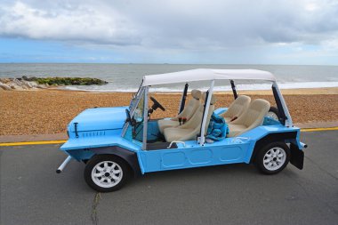 FELIXSTOWE, SUFFOLK, ENGLAND - MAYIS 04, 2025: Arka planda deniz kıyısındaki klasik açık mavi Mini Moke Parkı
