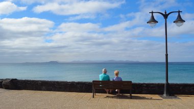 Playa Blanca Lanzarote Fuerteventura manzaraya bakarak bankta oturan yaşlı çift.