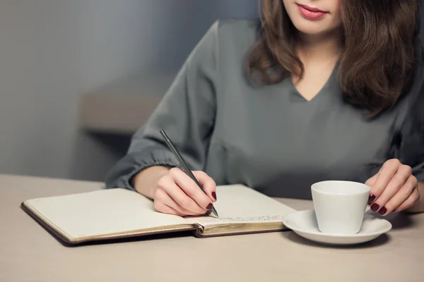 Hembra adulta joven tiene descanso de café en la cafetería y escribir notas en el diario o bloc de notas — Foto de Stock