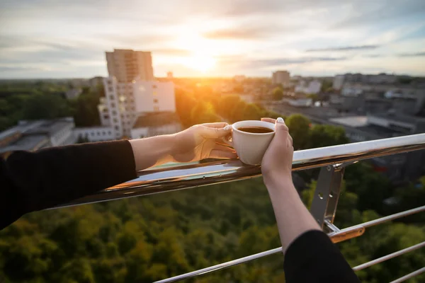 La mano della femmina tiene la tazza con caffè o tè in mano nei raggi del tramonto — Foto Stock