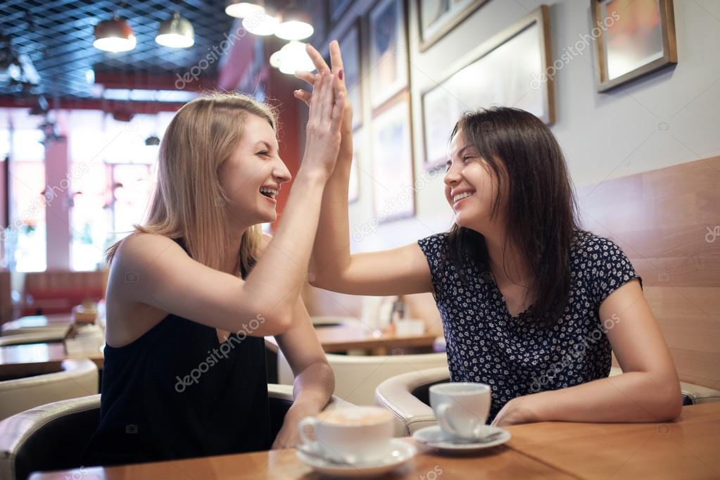 two happy girl friends have coffee in cafe and smiling;