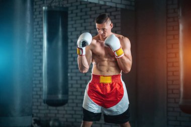 Güçlü sporcu boksör spor salonunda beyaz eldivenlerle egzersiz yapıyor.