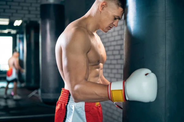 Vyčerpaný sportovec boxer odpočívá a opírá se o boxovací pytel po cvičení — Stock fotografie