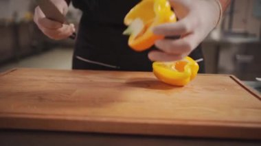 Şef aşçı, tıp eldivenleri içinde taze Yunan salatası için sarı biber doğruyor.