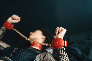 Şehvetli, kırmızı dudaklı, deri yakalı, boyunluk takan ve kelepçeli bir kadın.