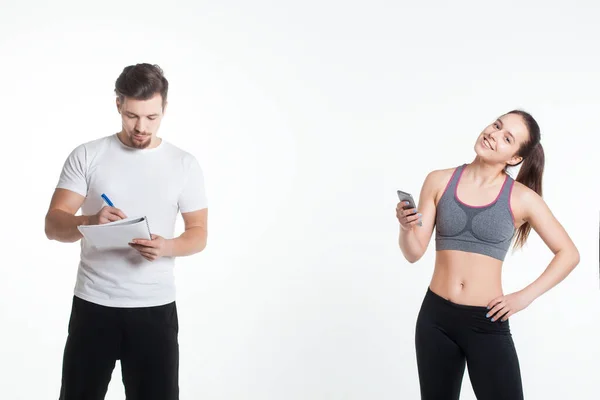 Entrenamiento femenino joven con entrenador de fitness personal en el teléfono inteligente aislado en línea — Foto de Stock