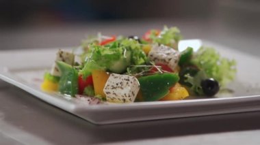Kare beyaz tabakta taze Yunan salatası ve baharatı yakın plan.