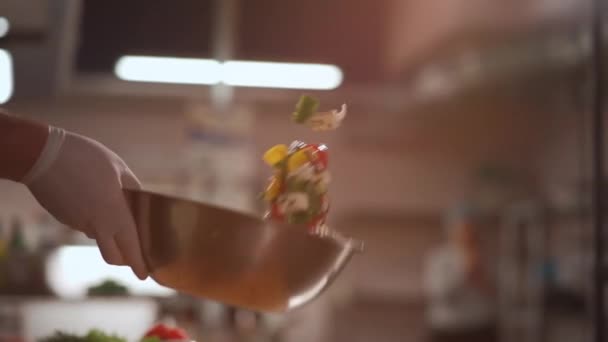 シェフは医療用手袋の混合物で手を調理するか、キッチンでボウルにギリシャサラダを投げる — ストック動画