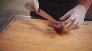 Şef aşçıya yakın çekim. Ellerinde tıbbi eldiven, taze salata için kırmızı soğan dilimliyor.