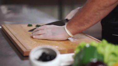 Şef aşçı, tıbbi eldiven giymiş taze sebze salatası için salatalık doğruyor.