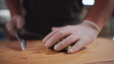 Şef aşçı, tıbbi eldiven giymiş taze sebze salatası için salatalık doğruyor.