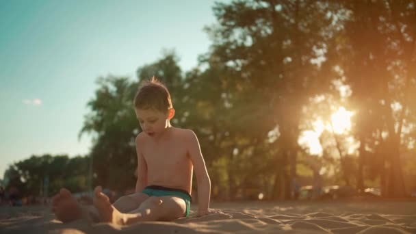 Glückliches Kind spielt mit Sand und wird im Sommerurlaub am Strand oder am Meer begraben — Stockvideo