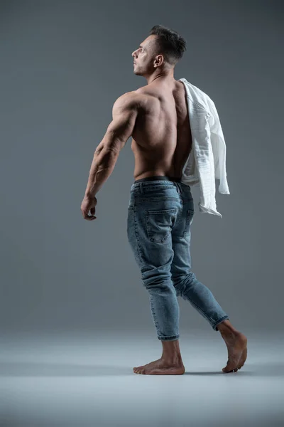 Young handsome man bodybuilder posing with perfect torso on grey background — Stock Photo, Image