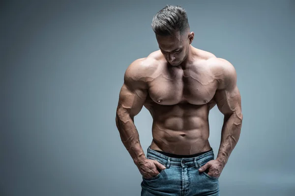 Jonge knappe sportman bodybuilder poseren in jeans op grijze achtergrond — Stockfoto