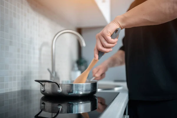 Gros plan de l'homme cuisine à la main dans une casserole avec cuillère en bois à la cuisine moderne de la maison — Photo