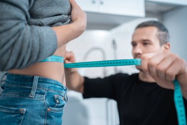 Fitness beslenme uzmanı erkek ölçü bandıyla kadın belini ölçer.