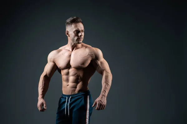 Joven deportista guapo culturista posando sobre fondo oscuro — Foto de Stock