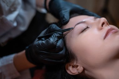 Güzel bir kadın kaş düzeltme operasyonunda cımbız kullanıyor.