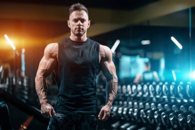 Kaslı vücutlu genç yakışıklı sporcu spor salonunda çalışıyor.