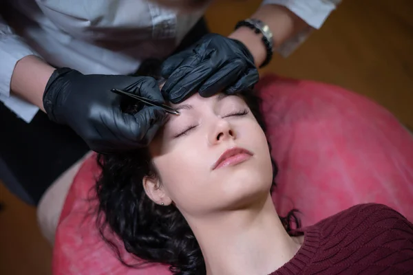 Bela fêmea em esteticista em procedimento de correção de sobrancelhas com pinças — Fotografia de Stock