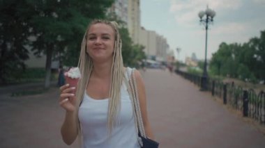 Parkta soğuk pembe dondurma yiyen örülmüş sarışın kadın.