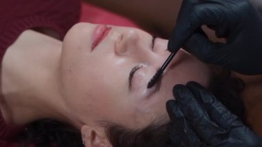 Güzellik salonunda kadın kaşlarını fırçayla tarayan eldiven giymiş bir güzellik uzmanı.